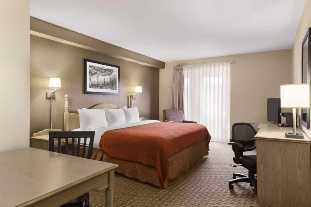A hotel room with a bed, desk, chair, and a television.