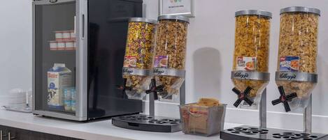 A breakfast station with a refrigerator, milk dispensers, and cereal dispensers.