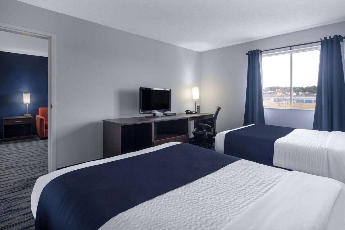 A hotel room with two beds, a desk with a TV, a chair, and a window with curtains.