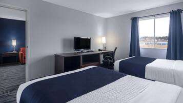 Habitación de hotel con dos camas, un escritorio, un televisor, una silla y una ventana con cortinas.
