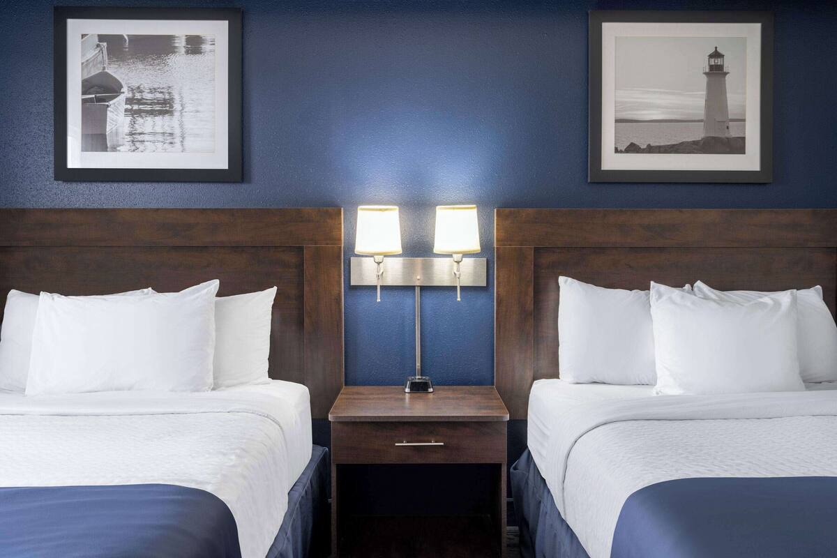 A hotel room with two beds, a nightstand with a lamp, and framed pictures on the wall.