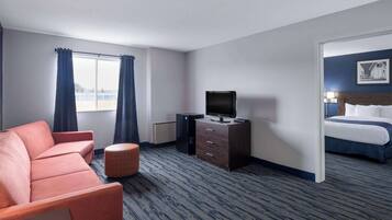 A hotel room with a sofa, a television on a wooden cabinet, a bed, and a view of the outdoors through a window.