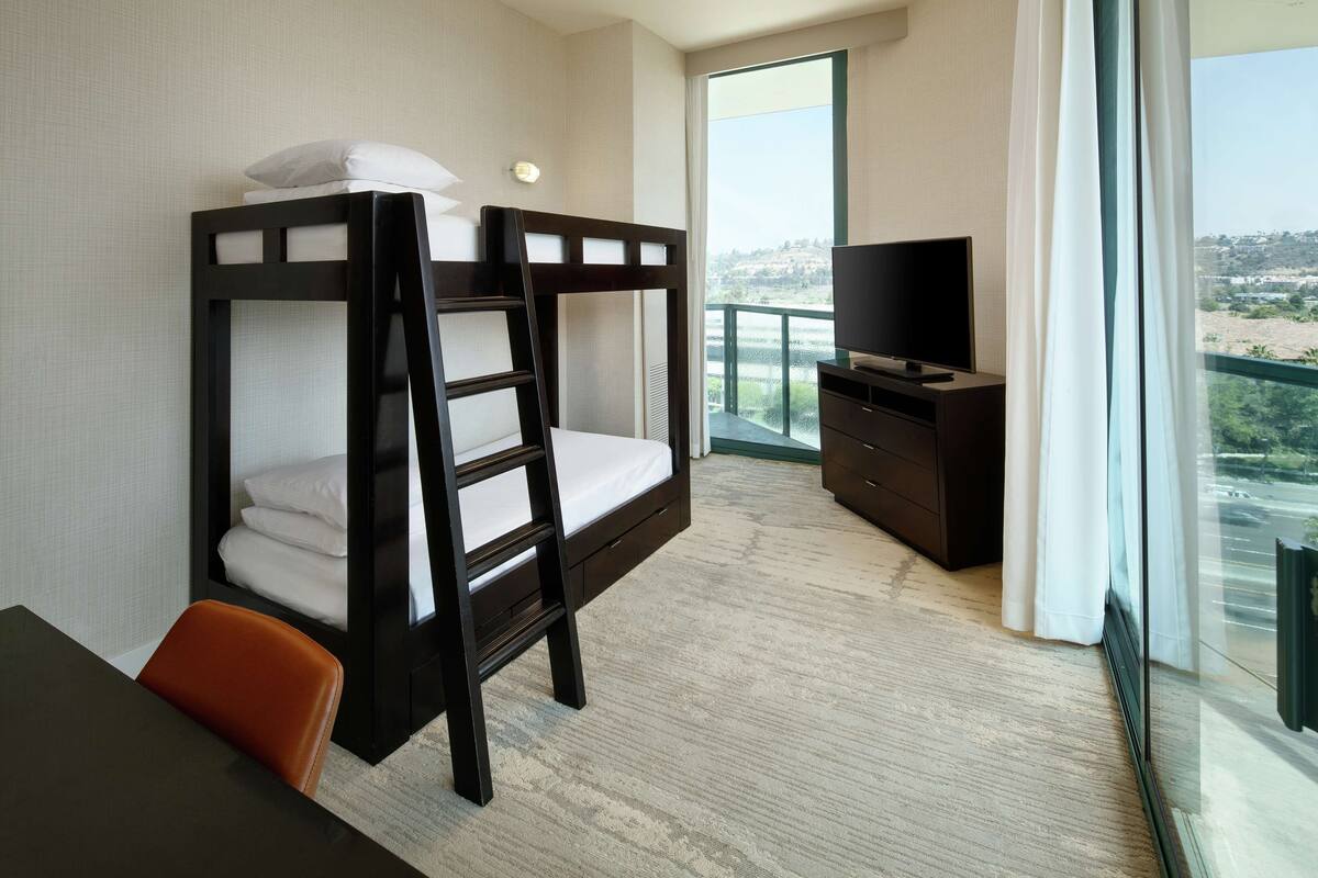 Et hotelværelse med køjesenge, tv, skrivebord og udsigt over byen.