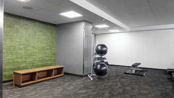A room with a green textured wall, a wooden bench, a metal rack with dumbbells, and a black exercise ball.