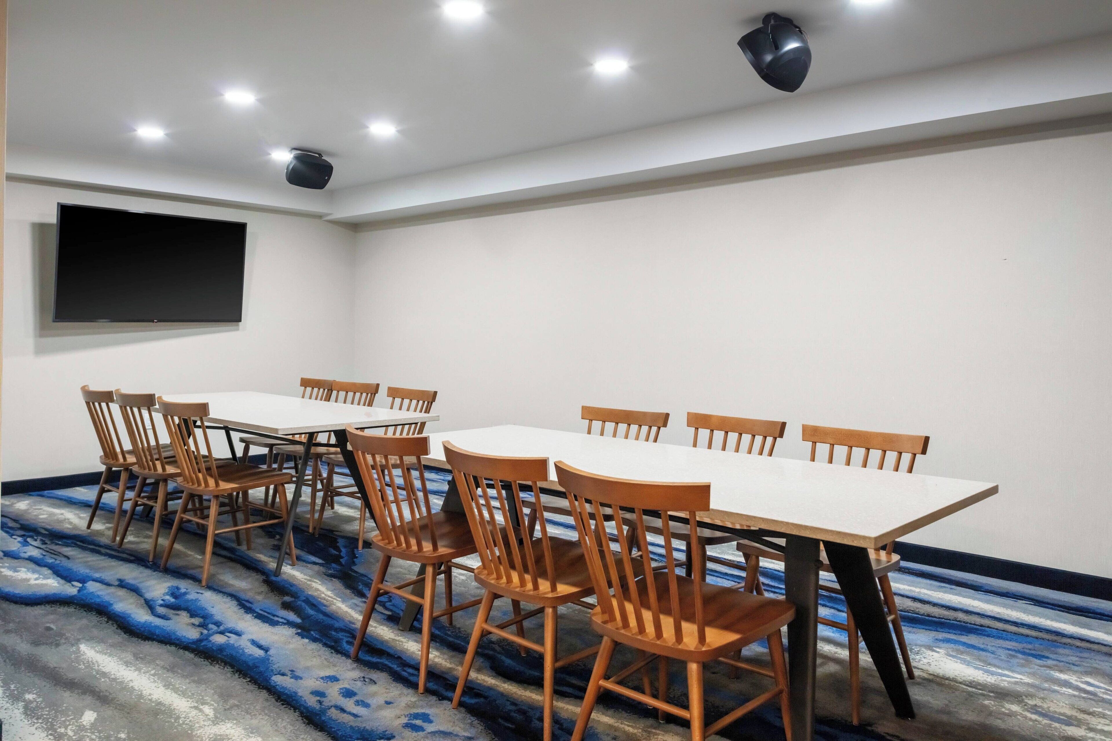 A conference room with a large table and chairs, a flat-screen TV, and ceiling lights.