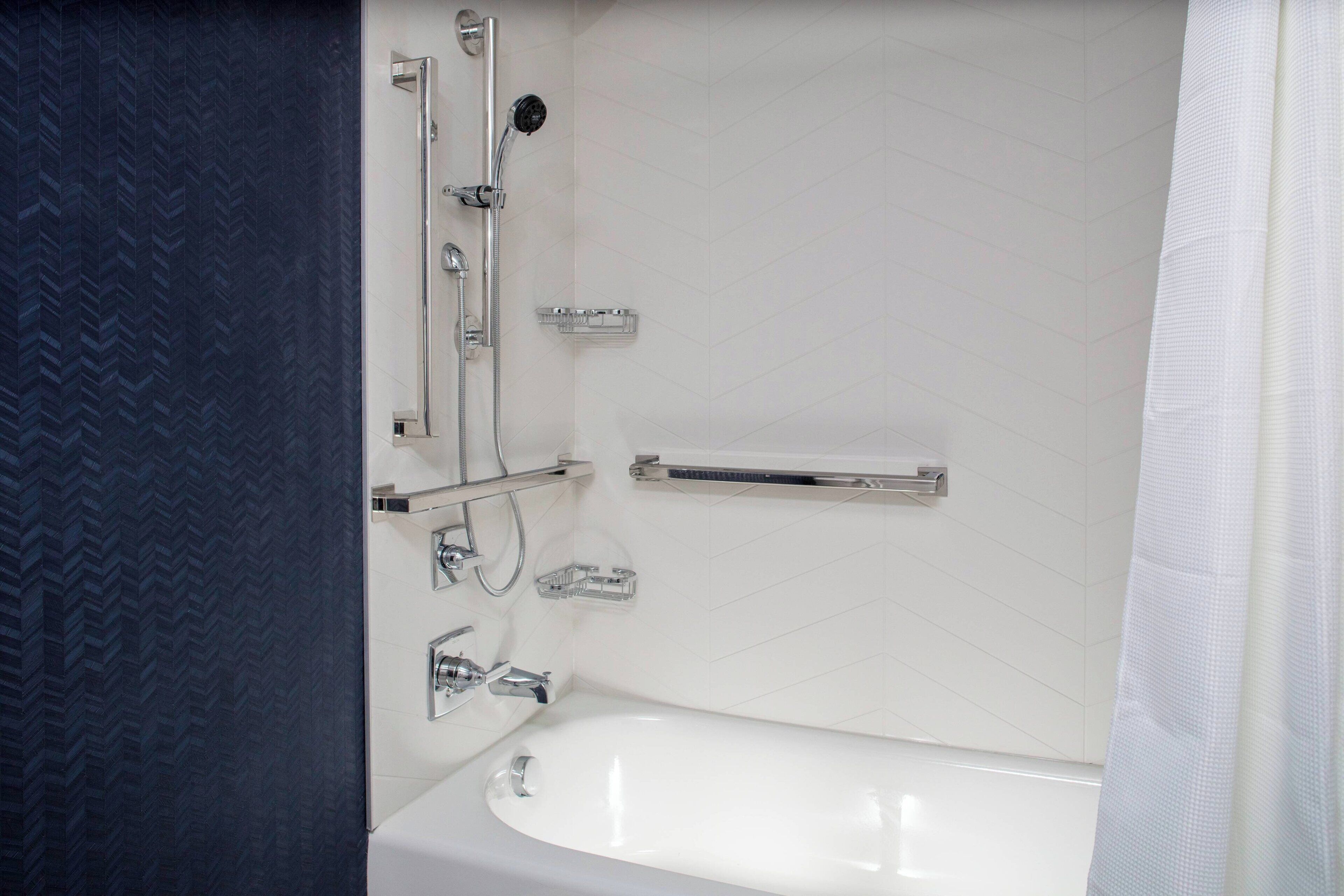 Une salle de bain moderne avec une baignoire blanche, des robinetteries chromées et une douche équipée d’un pommeau de douche à main.