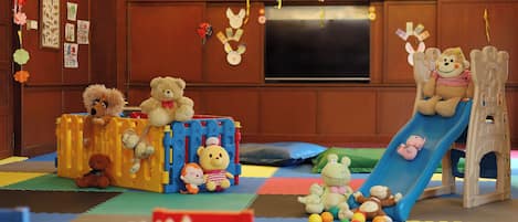 A playroom with a slide, play structures, and various stuffed animals.