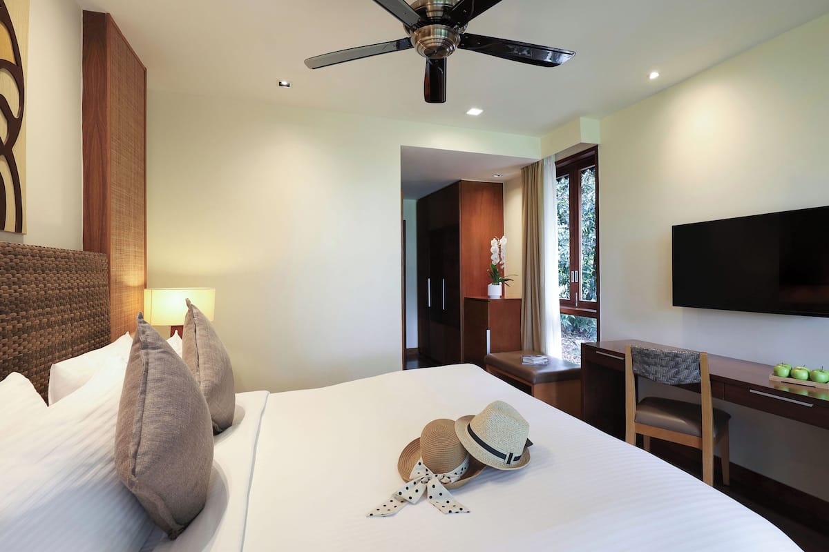 Ein Hotelzimmer mit Bett, Schreibtisch, Stuhl, Fernseher und Deckenventilator.