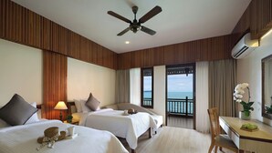 Une chambre d’hôtel avec deux lits, un ventilateur de plafond, une table avec une chaise et une vue sur la mer.