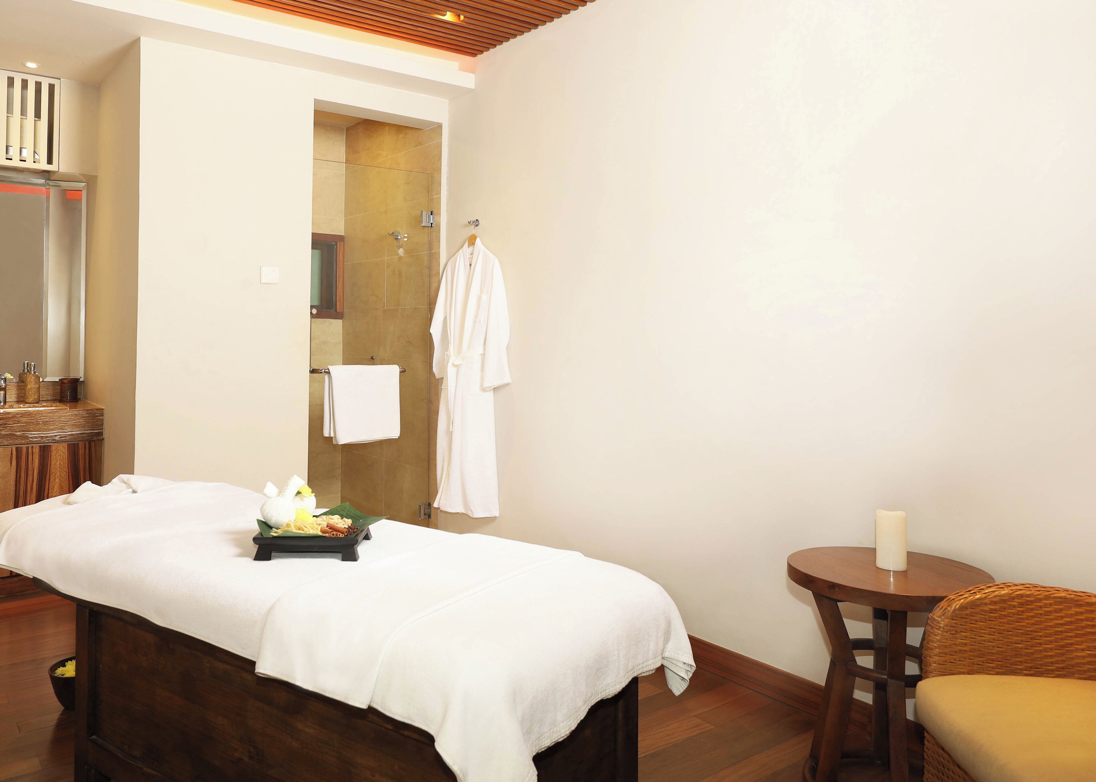 A spa room with a massage table, a small round table with a candle, and a wicker chair.