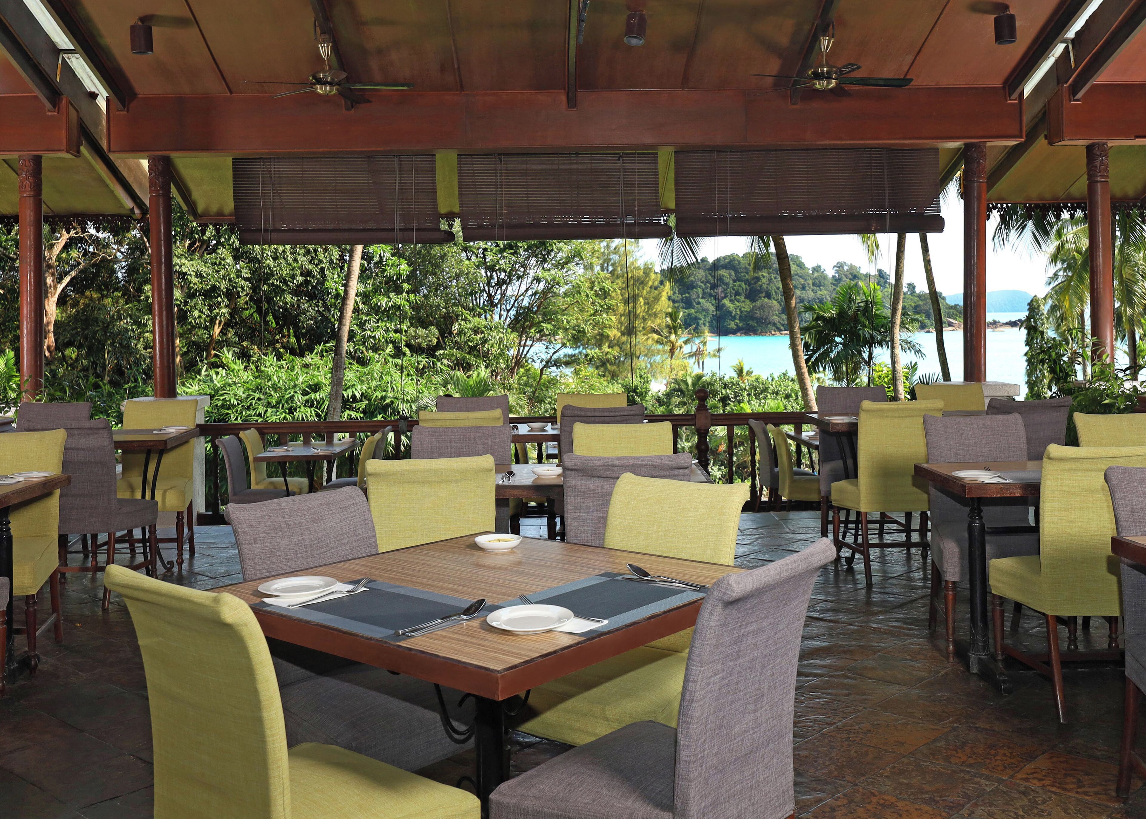An outdoor restaurant with tables and chairs, overlooking a scenic view of a body of water and lush greenery.