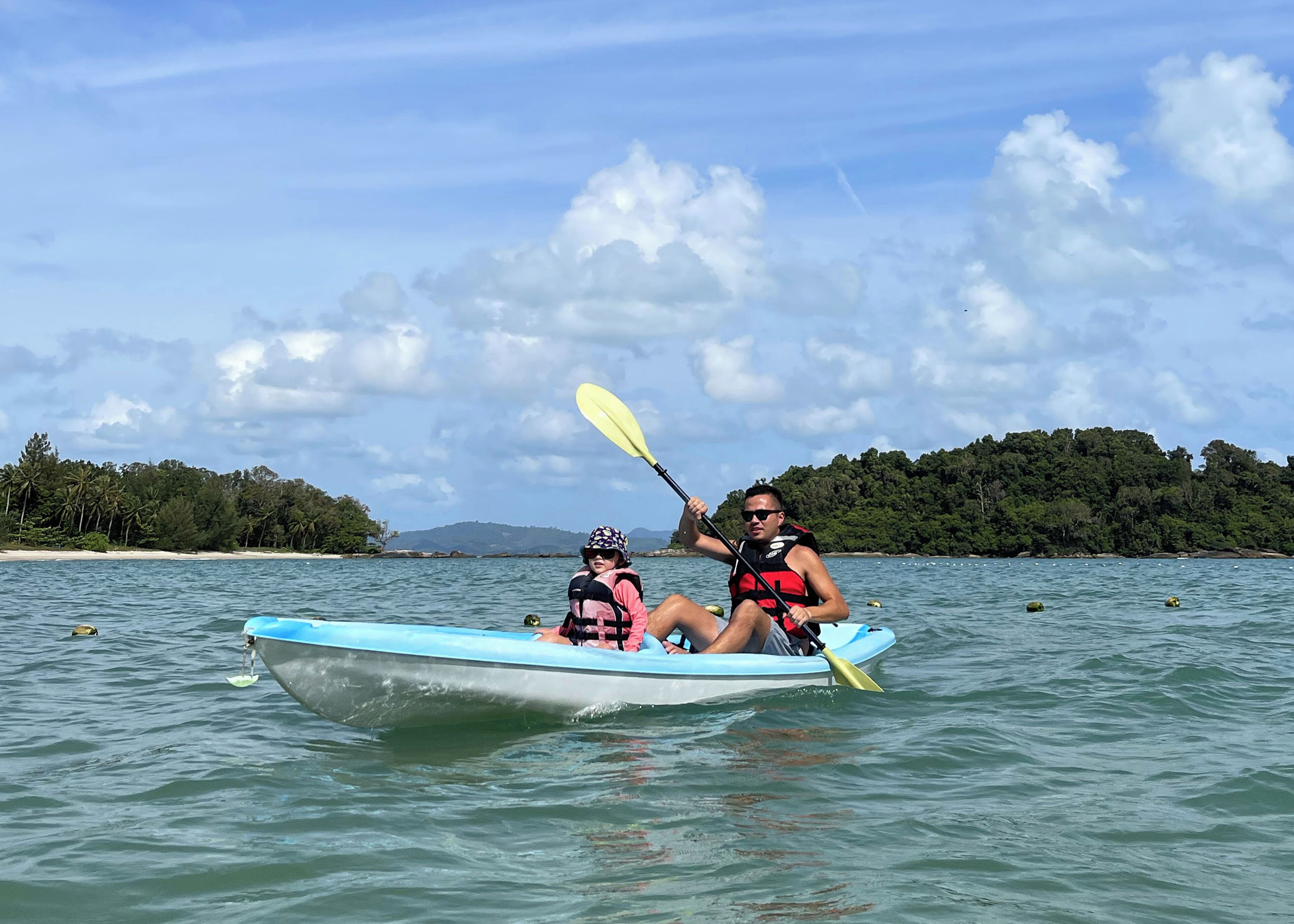 Two people kayaking on a calm body of water with a forested island in the background.