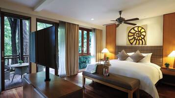 A hotel room with a bed, bedside table, lamp, and a view of trees through large windows.