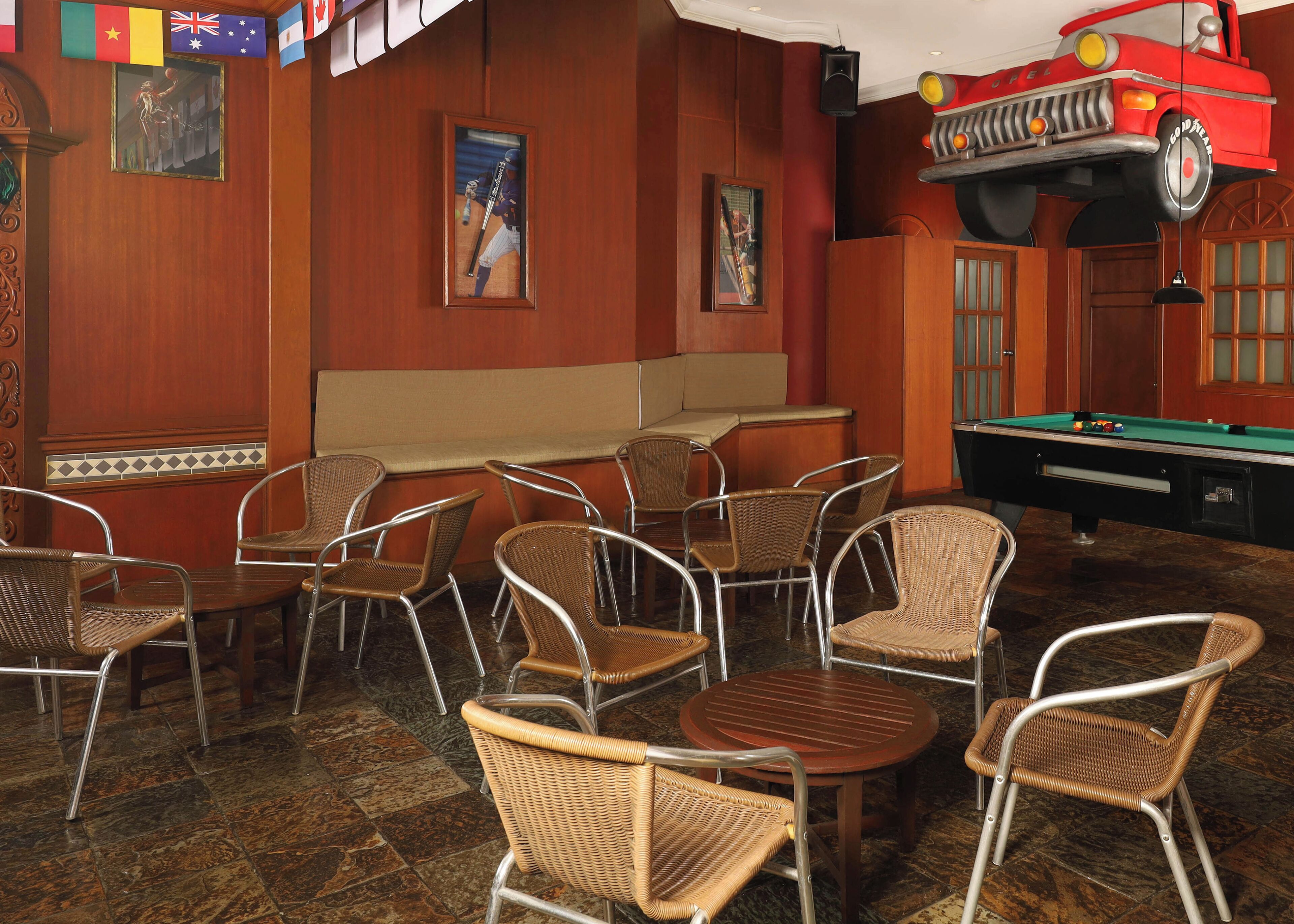A billiards room with wicker chairs, a pool table, and a red car decoration.