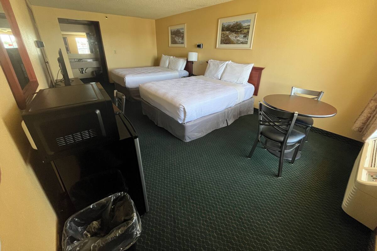 A hotel room with two beds, a desk, a chair, a table, and a trash bin.