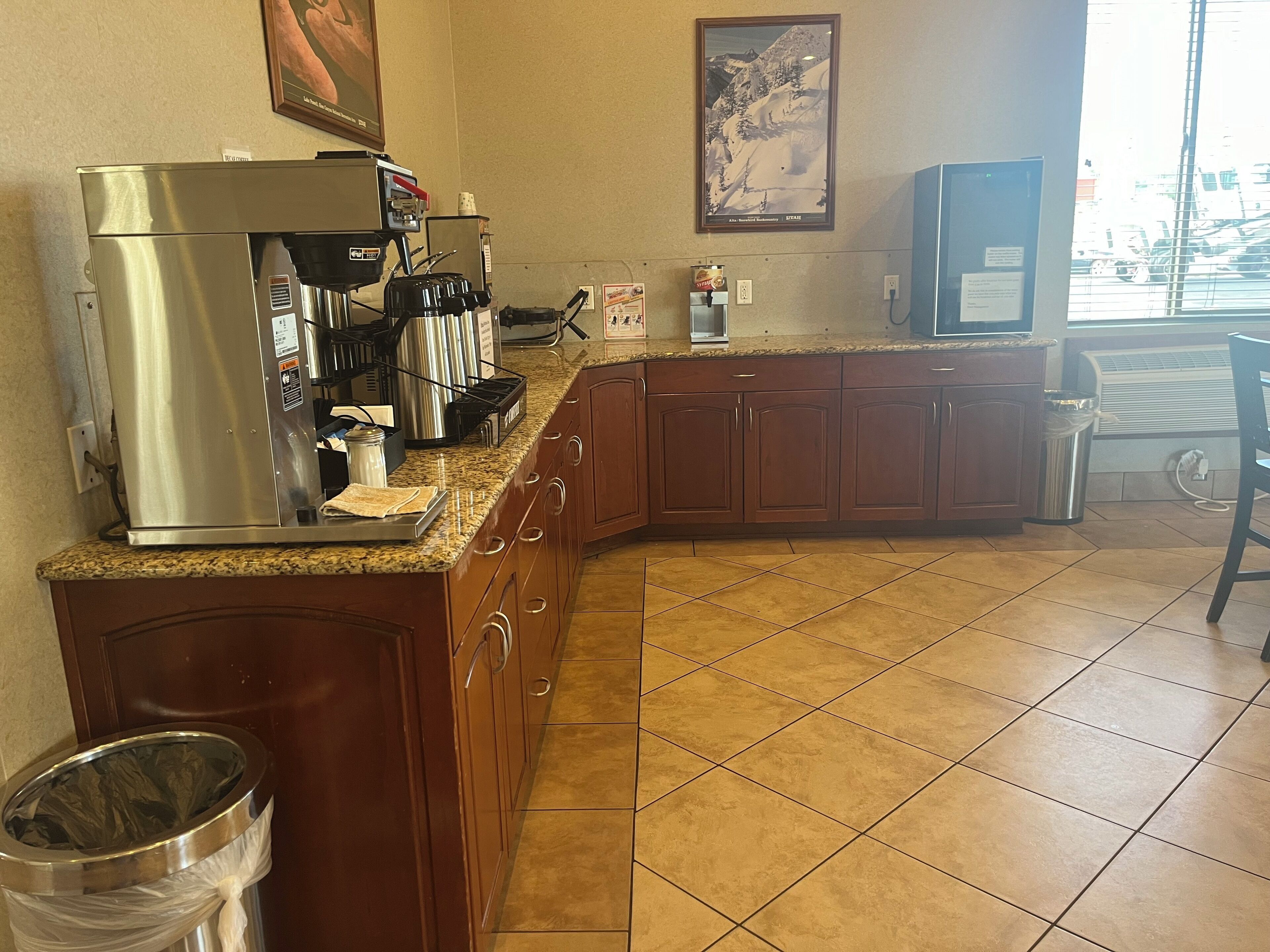 A kitchen with a stainless steel coffee maker, a trash can, and a window with a view of a snowy mountain.