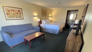 A hotel room with a blue sofa, a wooden desk, a bed with white linens, and two wall-mounted lamps. - National 9 Price (Price)