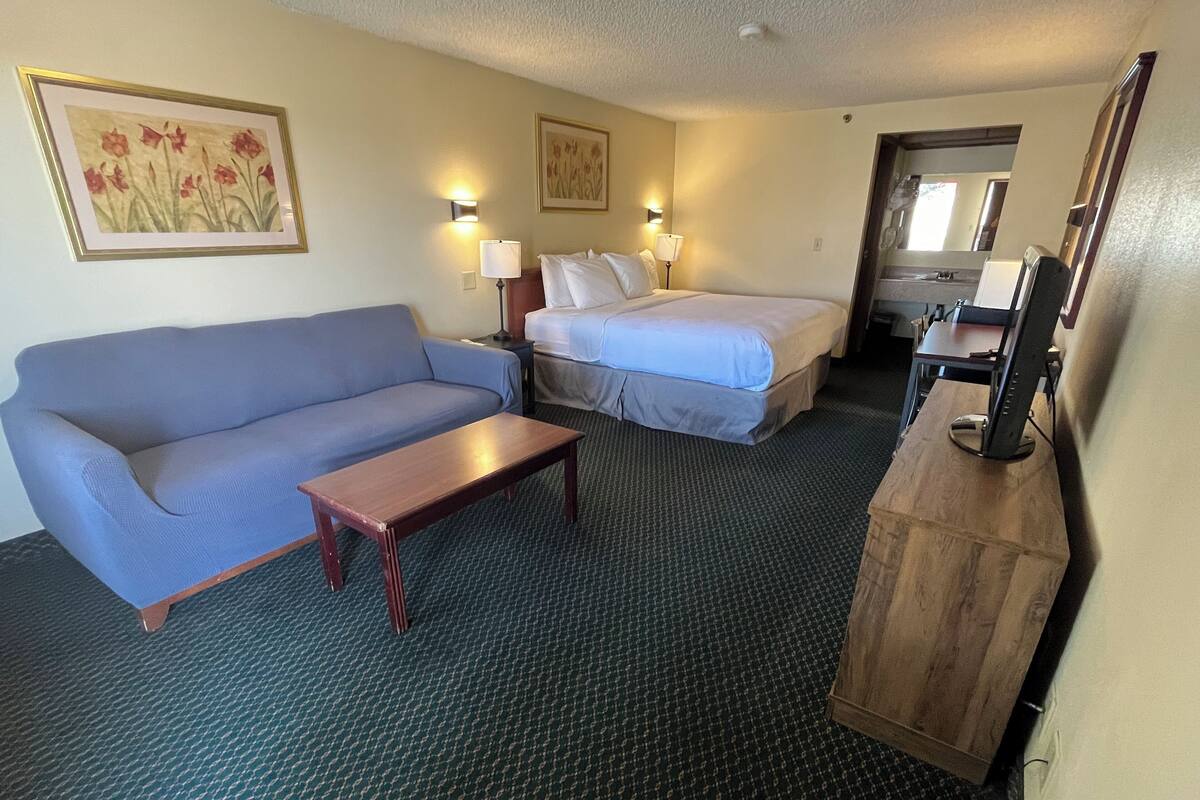 A hotel room with a blue sofa, a wooden desk, a bed with white linens, and two wall-mounted lamps.