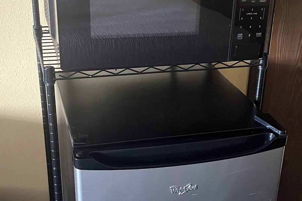 A compact Whirlpool microwave oven with a digital display, placed on a metal shelf against a beige wall.