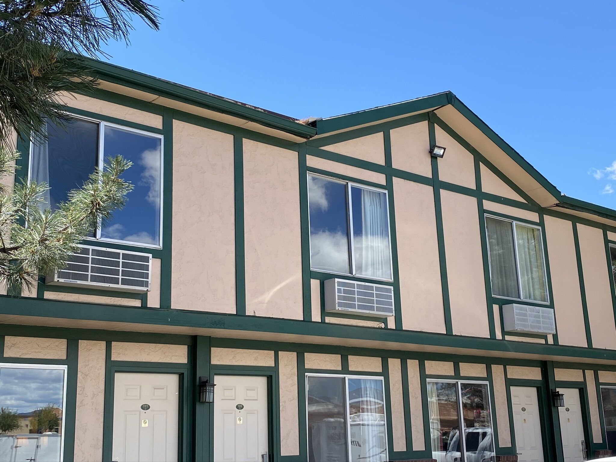A two-story building with a traditional architectural style, featuring a green and beige color scheme, multiple windows, and a visible air conditioning unit.