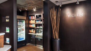 A modern interior with a dark wall, a large vase with sticks, and a refrigerator stocked with beverages. - Courtyard by Marriott Los Angeles Torrance Palos Verdes (Torrance)