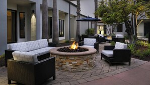 An outdoor patio with a stone fire pit, wicker furniture, and a view of the building's exterior. - Courtyard by Marriott Los Angeles Torrance Palos Verdes (Torrance)