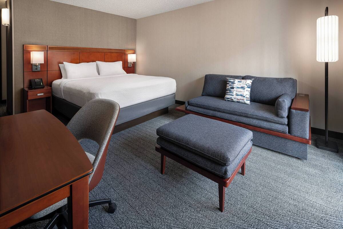 A hotel room with a bed, a sofa, a chair, a desk, and a lamp.