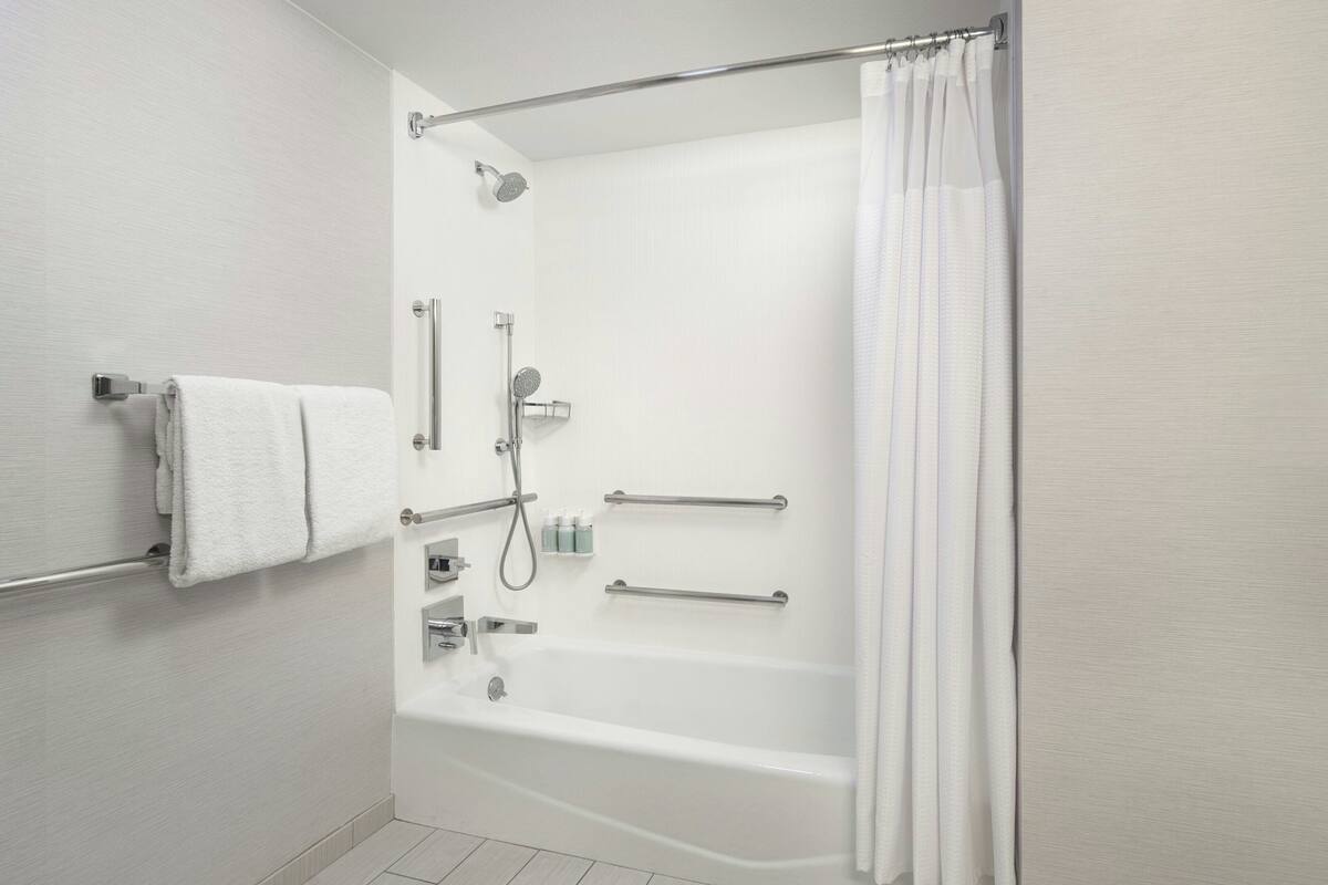 A modern bathroom with a bathtub, shower, and handrails.