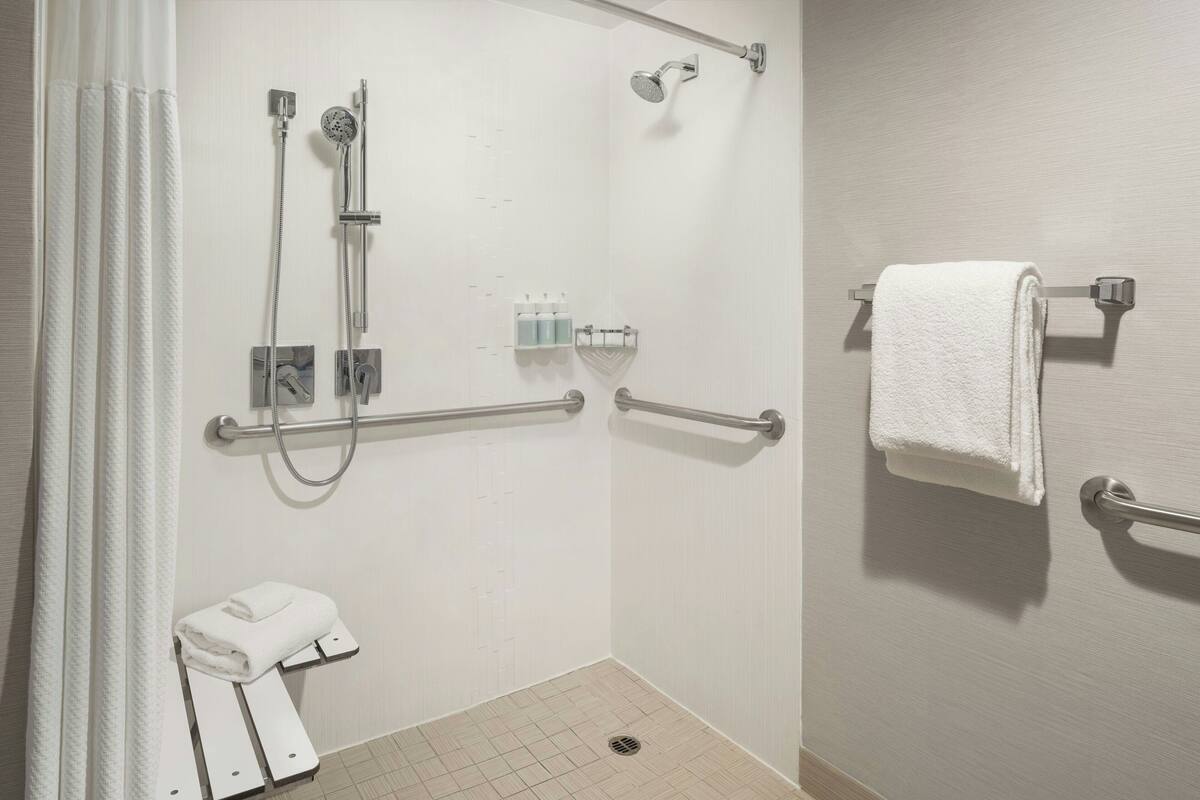 A bathroom with a shower, grab bars, a towel rack, and a toilet.