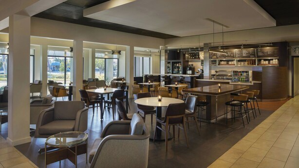 A modern hotel lobby with round tables, comfortable seating, a bar area, and a visible Starbucks sign. - Courtyard by Marriott Los Angeles Torrance Palos Verdes (Torrance)