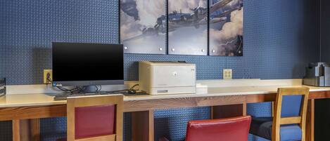 A room with a desk, a computer, and a television. There are two red chairs and a blue chair. A large painting of an airplane is on the wall.