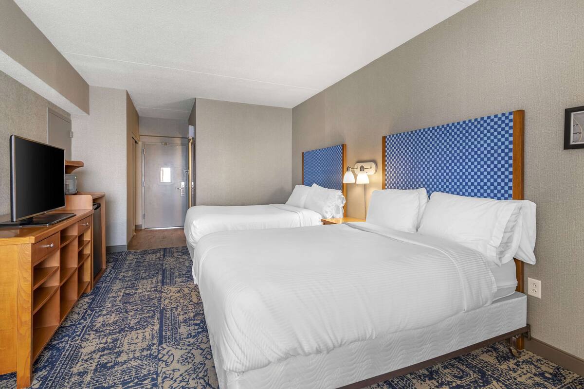 A hotel room with two beds, a TV, a desk, and a patterned rug.