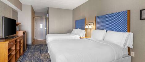A hotel room with two beds, a TV, a desk, and a patterned rug.