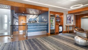 A reception area with a wooden reception desk, a blue wall with an 'Aviator' sign, a refrigerator stocked with beverages, and a seating area with a unique chair.