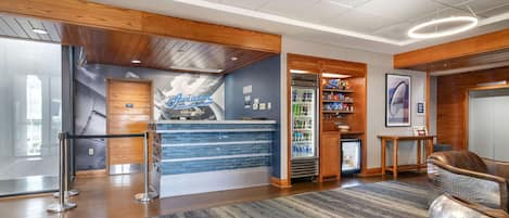 A reception area with a wooden reception desk, a blue wall with an 'Aviator' sign, a refrigerator stocked with beverages, and a seating area with a unique chair.