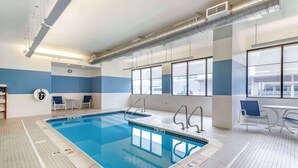 An indoor swimming pool with clear lane markings, a lifeguard chair, and a seating area with chairs and a table.