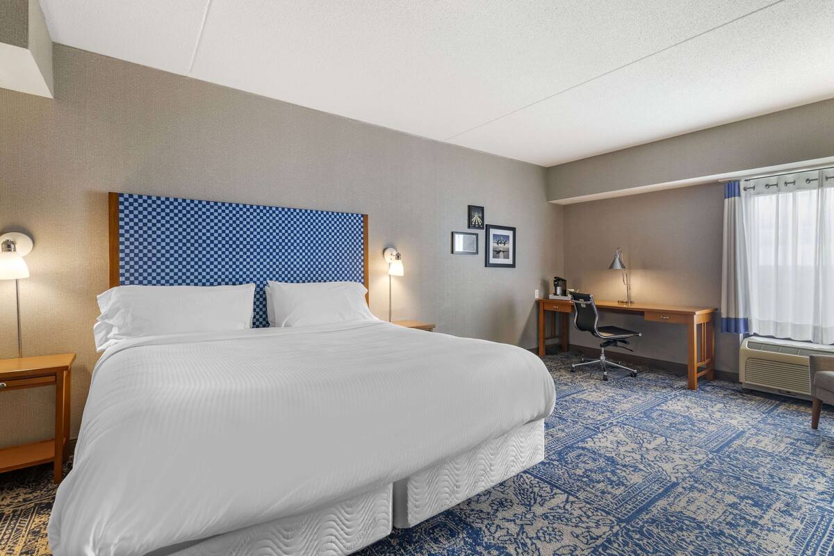 A hotel room with a large bed, a desk, a chair, and a window with curtains.