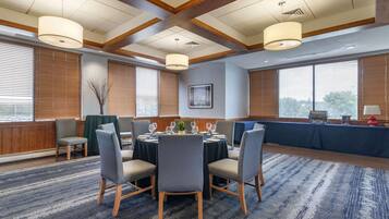 A conference room with a round table, four chairs, and a large window with blinds.