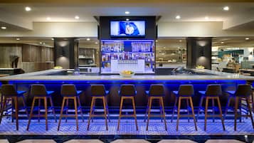 A bar area with a long counter, multiple stools, and a television screen above.