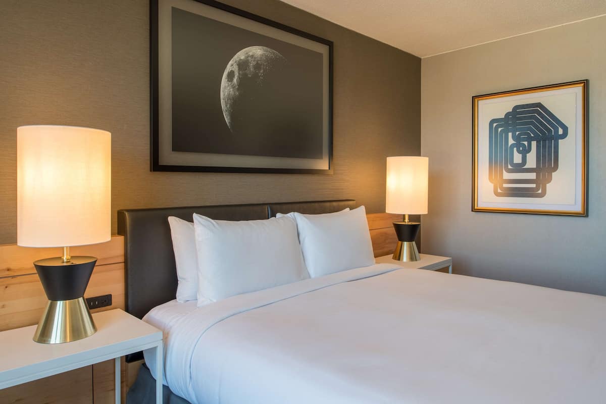 A hotel room with a large bed, two bedside tables with lamps, a framed picture of a crescent moon, and a framed abstract artwork.