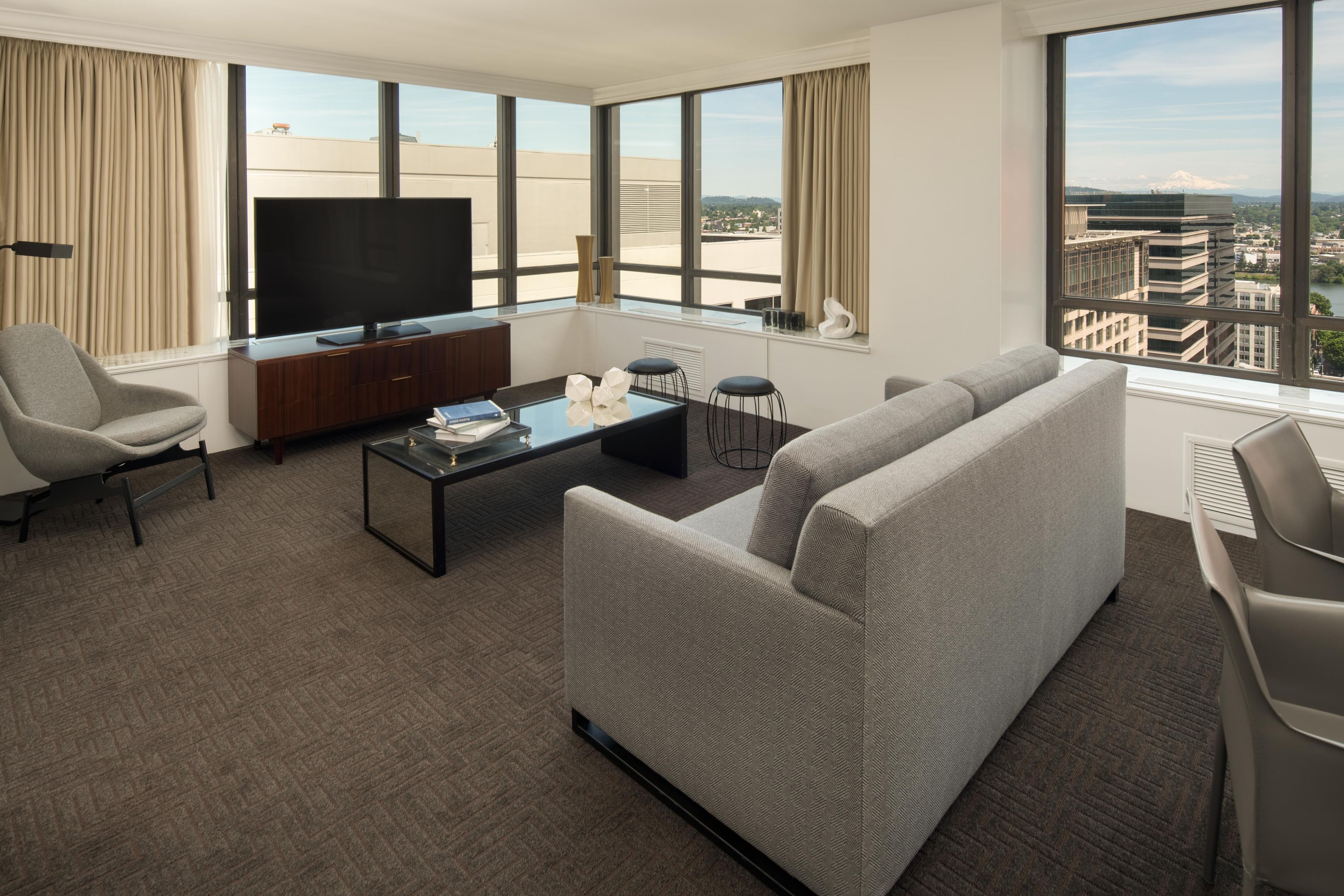 Habitación de hotel moderna con una gran televisión de pantalla plana, un sofá, una mesa de centro y vistas a la ciudad.