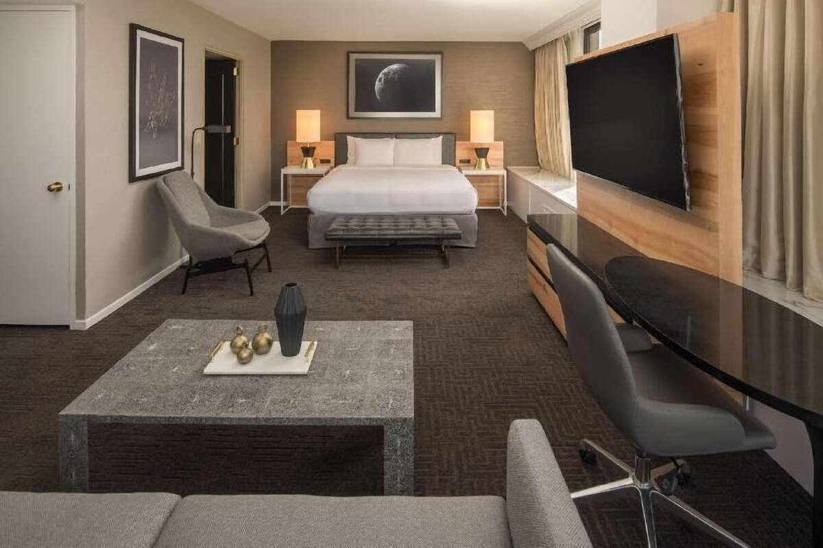 A hotel room with a bed, two bedside lamps, a TV, a chair, a coffee table with decorative items, and a couch.