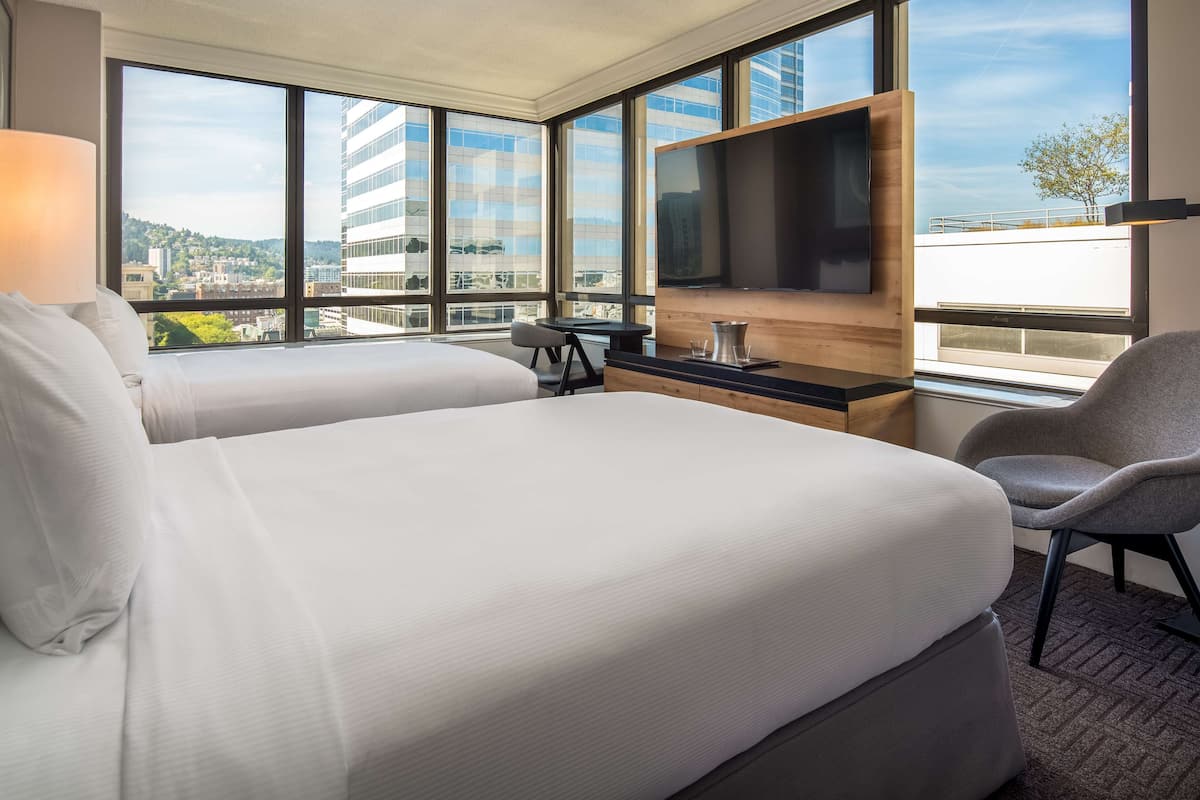 A hotel room with two beds, a TV, a desk, and a chair.