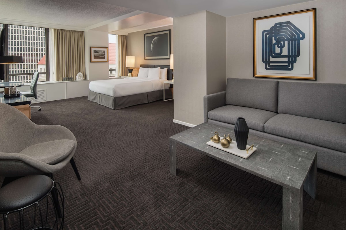 A hotel room with a bed, a sofa, a coffee table, and a desk with a chair.
