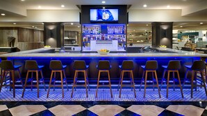 A bar area with a long counter, multiple stools, and a television screen displaying the NFL logo. - Hilton Portland Downtown (Portland)