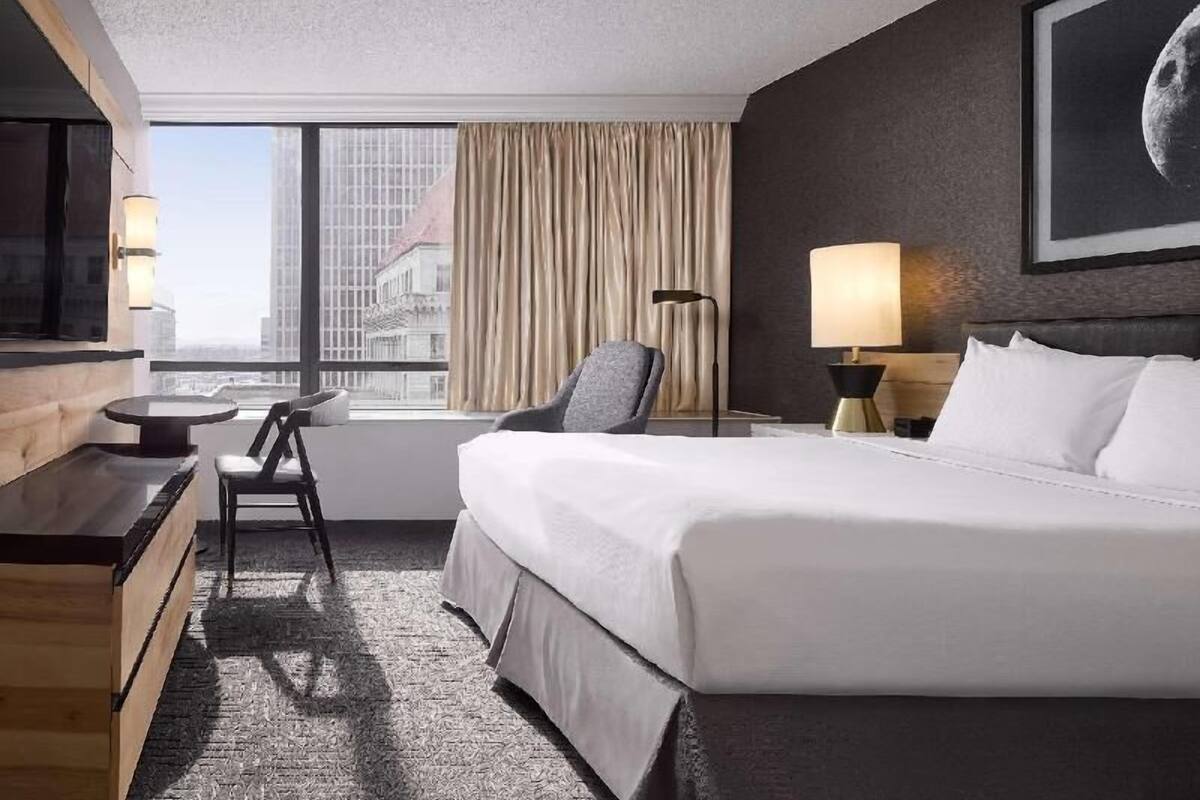 A hotel room with a bed, a desk, a chair, a lamp, a TV, and a window with curtains.