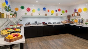 A modern kitchen with white tiled walls, black cabinets, and a variety of fruits and breakfast items on the counter.