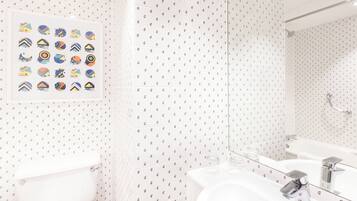 Un baño con inodoro, lavamanos y espejo. Hay un cartel con varios diseños en la pared.