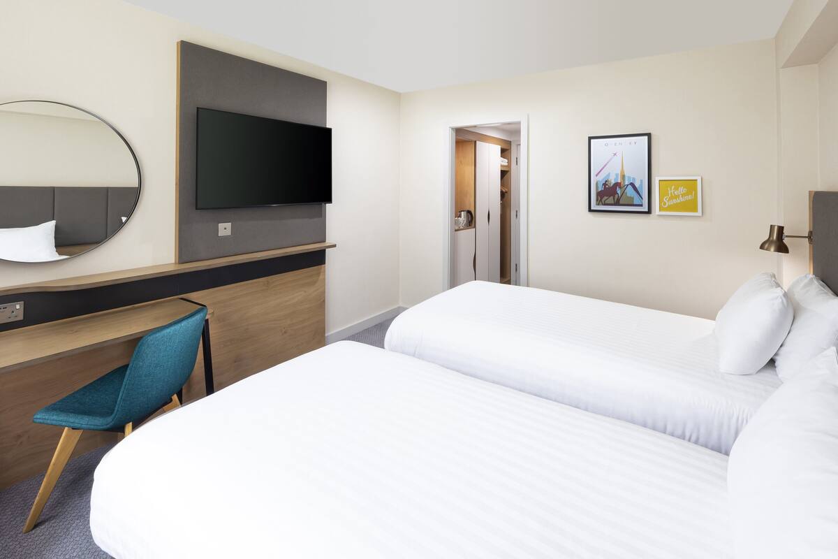 A hotel room with a bed, a desk with a chair, a TV, and a door leading to a bathroom.