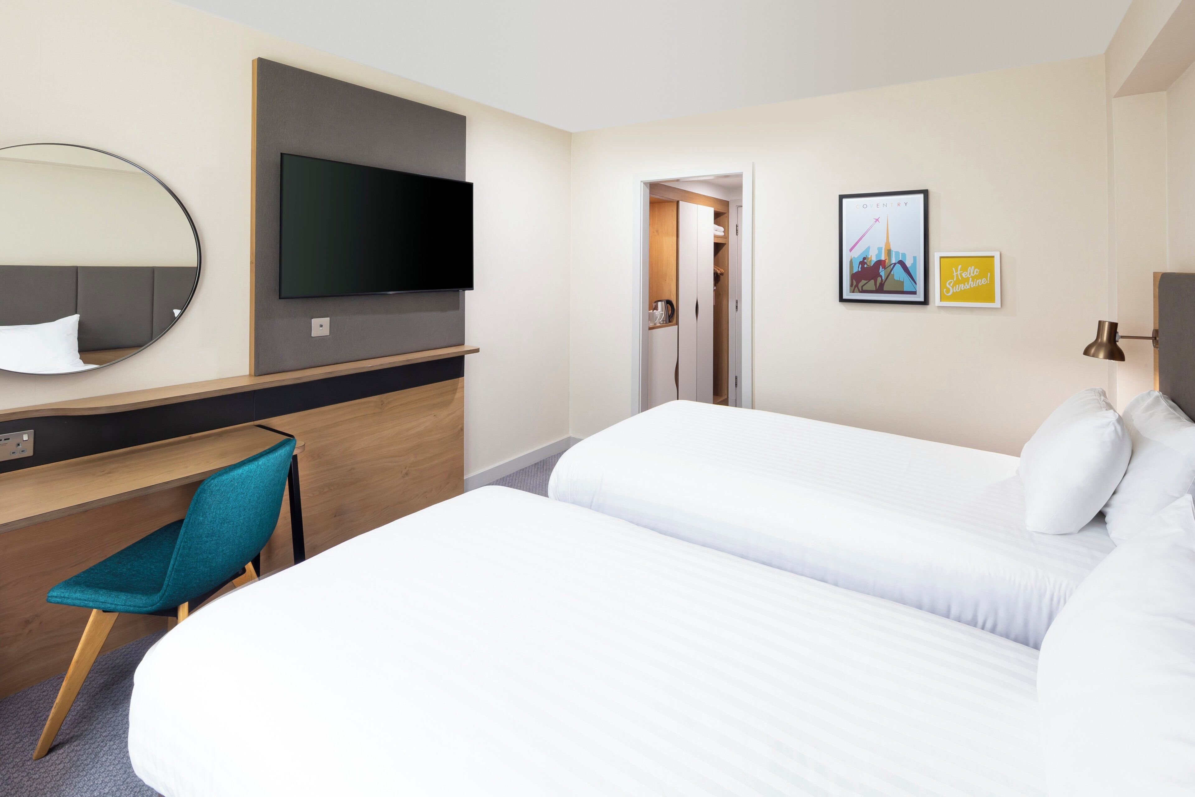 A hotel room with a bed, a desk with a chair, a television, and a door leading to another room.